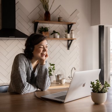 Eine junge Frau lehnt am Küchentresen und schaut auf ihren Laptop.