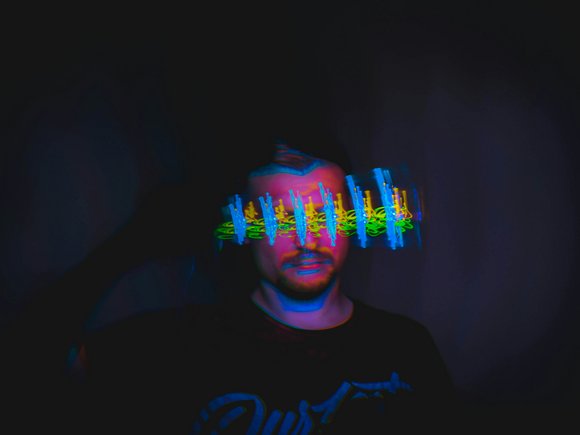Ein Mann im dunkeln. Vor seinem Gesicht bunte Farbblitze.
