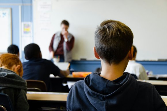 Blick über die Schulter eines Schülers durch den Raum zur Lehrkraft.
