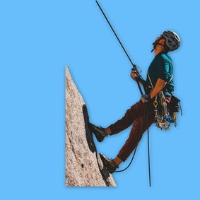 Eine Person mit Sicherheitsausrüstun klettert am Seil eine Bergwand hinauf