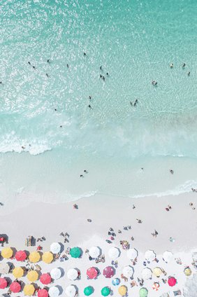 Blick von oben auf einen mt Menschen und Schirmen gefüllten Sandstrand.