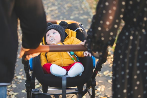 Zwei Personen schieben einen Kinderwagen mit einem Baby.