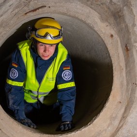 Eine Person in Ausrüstung des Technischen Hilfswerks kriecht durch einen Tunnel.