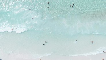 Blick von oben auf einen mt Menschen und Schirmen gefüllten Sandstrand.
