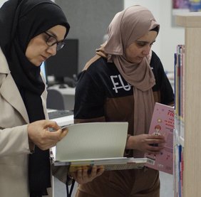 Zwie Teilnehmerinnen durchsuchen eines der Regale und blättern durch Bücher.