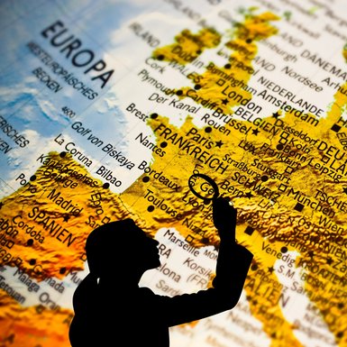 Der Schatten eine Frau sucht mit einer Lupe den Europäischen Kontinent in einem Atlas ab.