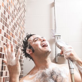 Bild: Miguel Tamayo - stock.adobe.com Ein Mann steht eingeseift unter der Dusche und singt in die Handbrause