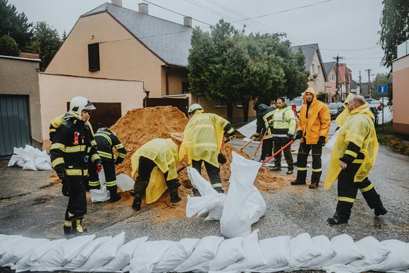 Menschen un Feuerwehruniformen befüllen und stapeln Sandsäcke