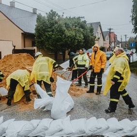 Menschen un Feuerwehruniformen befüllen und stapeln Sandsäcke