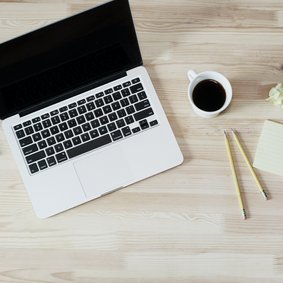 Ein laptop, eine Kaffeetasse und ein Notizblock mit Stiften.