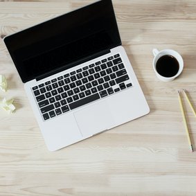 Ein laptop, eine Kaffeetasse und ein Notizblock mit Stiften.