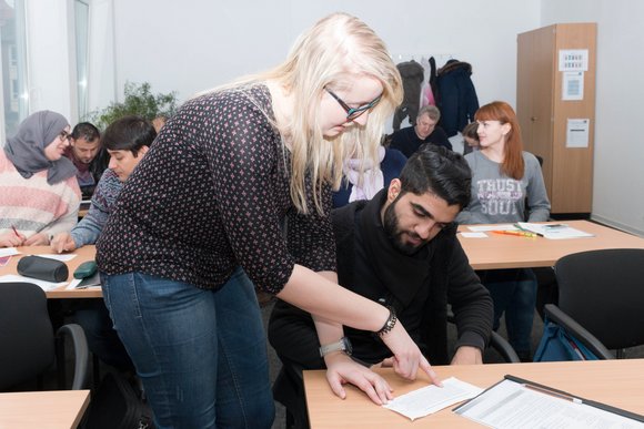 Ein Klassenraum im Deutschunterricht. Die Dozentin erklärt einem Teilnehmer eine Aufgabe. Bild: Gamze Coruh.