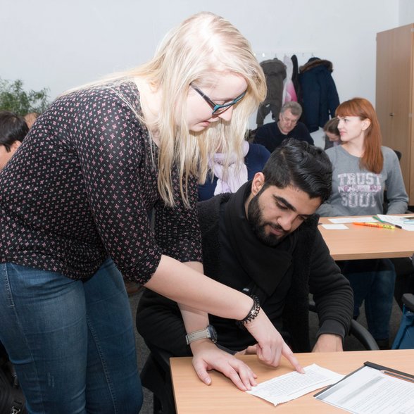 Menschen in einem Unterrichtsraum. Die Dozentin erkärt einem Mann eine Aufgabe. Bild: Gamze Coruh.