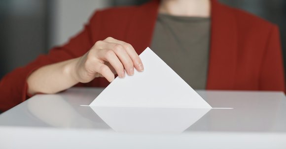 Nahaufnahme einer Person, die einen Stimmzettel in eine Wahlurne steckt.