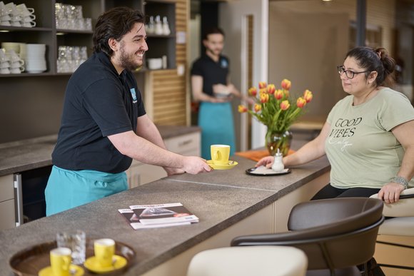 Ein Teilnehmer der Oldenburger Jugendwerkstatt serviert einem Gast einen Kaffee im Esscampo.