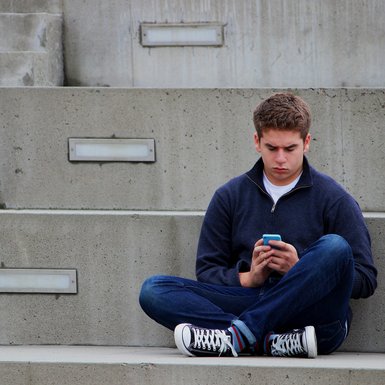 Ein Jugendlicher sitzt auf einer Treppe und schaut auf sein Smartphone.