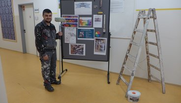 Ein junger Mann in Arbeitskleidung neben einer Leiter.