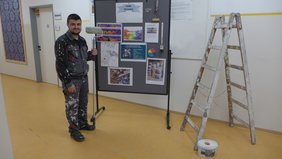 Ein junger Mann in Arbeitskleidung neben einer Leiter.