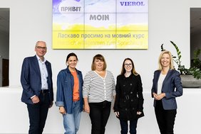 VHS-Geschäftsführer Andreas Gögel und Mirja Viertelhaus-Koschig, Vorstandsvorsitzende der VIEROL AG mit einer Dozentin und zwei Teilnehmerinnen de MiA-Kurse im Foyer des VIEROL-Gebäudes. Im Hintergrund begrüßt auf einer großen LED-Leinwand ein Bild in Deutsch und Ukrainisch die Teilnehmerinnen. Bild: VIEROL AG.