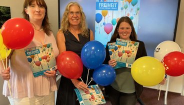 Drei Frauen die das neuen Programmheft hochhalten und bunte Ballons festhalten