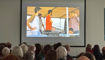 Blick über das Podium auf die Leinwand mit einer Szene aus dem Film.