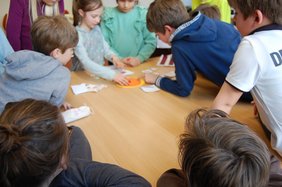 Kinder stehen rund um einen Tisch und spielen. Bild: VHS Hatten und Wardenburg