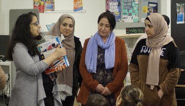 Eine Mitarbeiterin der Bibliothek erklärt Teilnehmerinnen anhand eines Buchrückens die Einteilung der Bibiliothek in Farben.