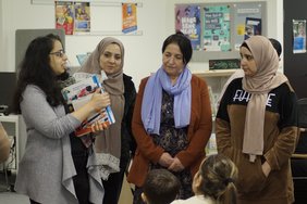 Eine Mitarbeiterin der Bibliothek erklärt Teilnehmerinnen anhand eines Buchrückens die Einteilung der Bibiliothek in Farben.