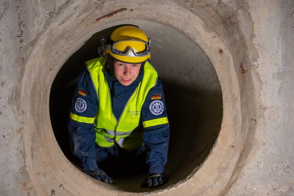 Eine Person in Ausrüstung des Technischen Hilfswerks kriecht durch einen Tunnel.
