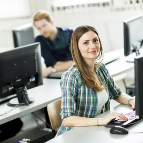 Junge Menschen sitzen in einem Seminarraum an PCs.