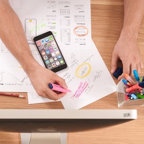 Eine Person an einem Bildschirm markiert etwas auf Papier