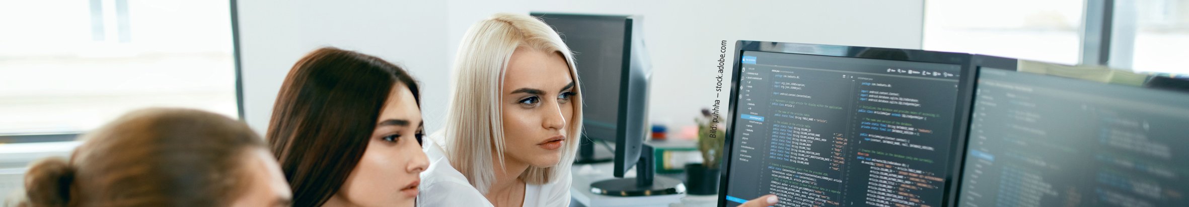 Bild: puhhha – stock.adobe.com Drei junge Menschen sitzen vor einem PC mit Code und unterhalten sich.