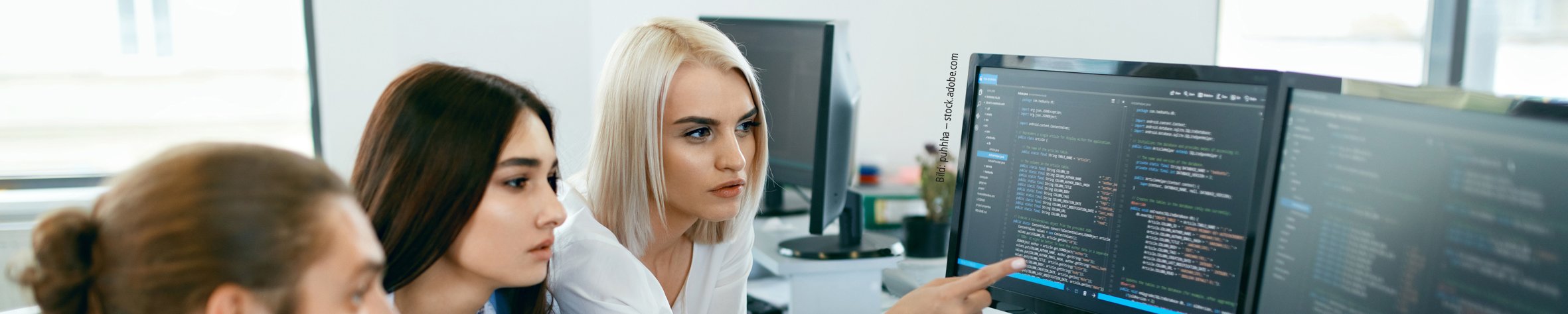 Bild: puhhha – stock.adobe.com Drei junge Menschen sitzen vor einem PC mit Code und unterhalten sich.