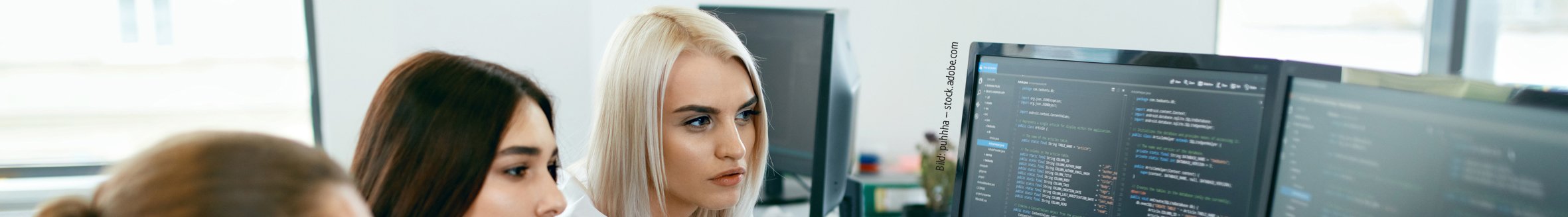 Bild: puhhha – stock.adobe.com Drei junge Menschen sitzen vor einem PC mit Code und unterhalten sich.