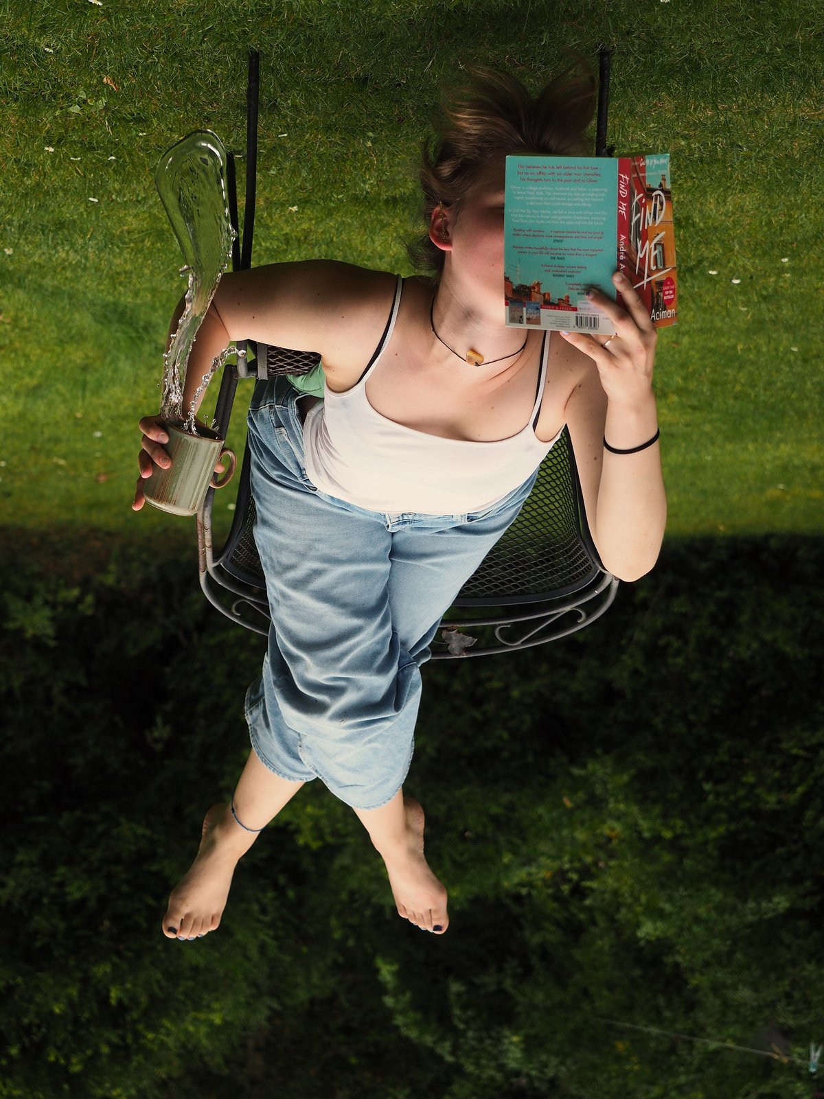 Bild: Malin Reisdorff. Eine junge Frau liegt kopfüber auf einem Stuhl und liest. Aus einer Tasse in ihrer Hand spritzt eine Flüssigkeit.