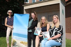 Das Team der VHS-Außenstellen sitzt in einem Strandkorb und hält das Programmheft in der Hand. Bild: Marén Bettmann, NWZ.