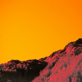Eine Landschaft in verfremdeten Farben: Ein roter Hügel vor einem oragenen Himmel..