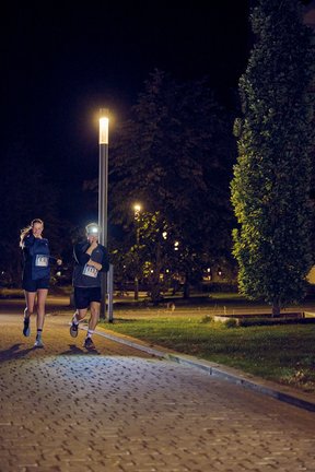 Eine junge Frau und ein junger Mann laufen im Dunkeln und halten ihre Hände in Denkerpose unter das Kinn.