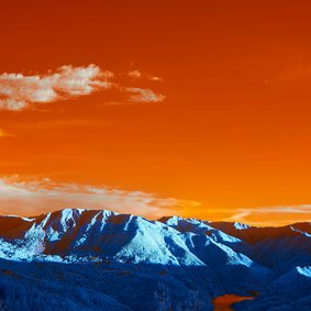 Eine Landschaft in verfremdeten Farben: Blaue Berge vor einem oragenen Himmel.