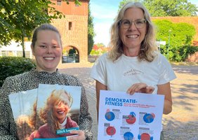 Katharina Janßen und Katja Ratje vor dem Glockenturm mit dem VHS-Programmheft