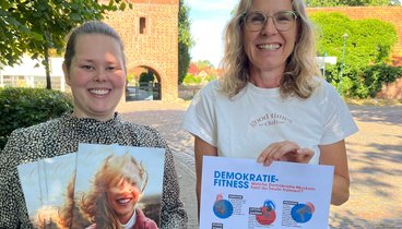 Bild: NWZ Katharina Janßen und Katja Ratje vor dem Glockenturm mit dem VHS-Programmheft