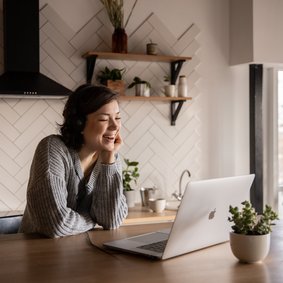 Eine junge Frau lehnt am Küchentresen und schaut auf ihren Laptop.
