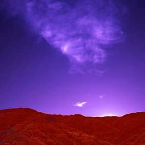 Eine Landschaft in verfremdeten Farben: Ein roter Hügel vor einem lilanen Himmel.