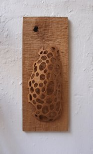 „Nu Bubbles I“ ist eine Wandskulptur aus Eiche. Auf einem Brett ist ein gewölbtes Oval mit zahlreichen Löchern platziert.