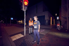 Eine Läuferin wartet an einer roten Ampel. Im Hintergrund wartet ein Streckenposten.