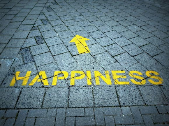 Bild: Unsplash Schriftzug Happiness mit einem Pfeil nach oben auf einer Straße.