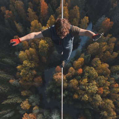 Eine Person balanciert auf einem Hochseil über einem Wald.
