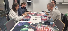 Vier Personen spielen gemeinsam an einem Tisch ein Rollenspiel.
