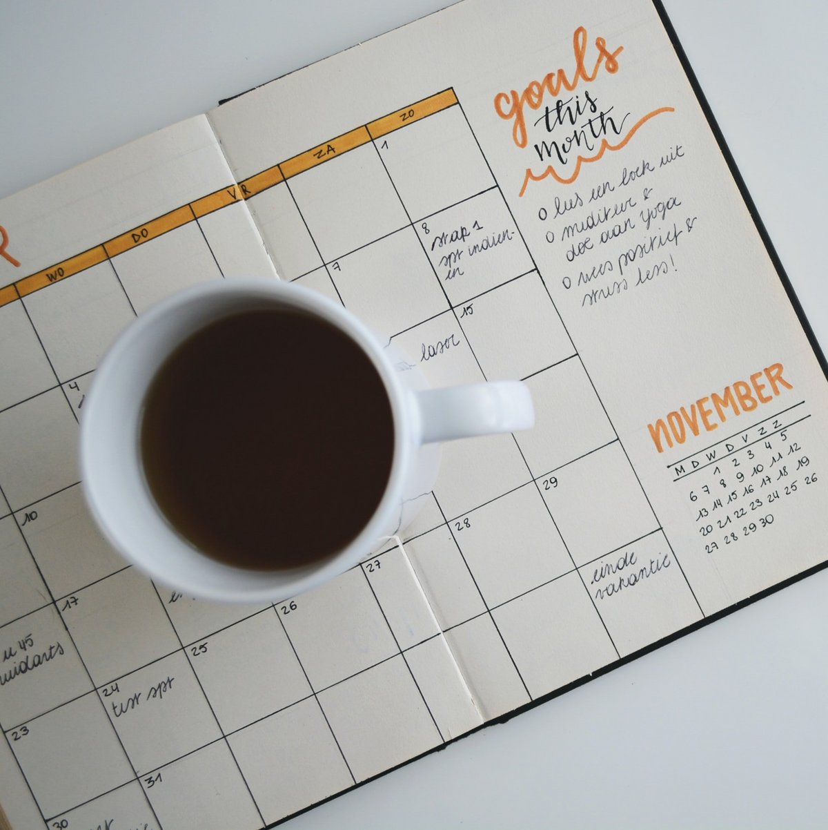 Ein Notizbuch mit Zielen für den Monat November liegt geöffnet auf einem Tisch. Auf dem Planer steht eine Tasse Kaffee.