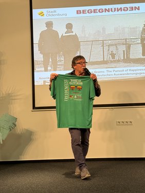 Dr. Grams hält ein T-Shirt das anlässlich eines Festes der Stadt Oldenburg in Indiana bedruckt wurde.